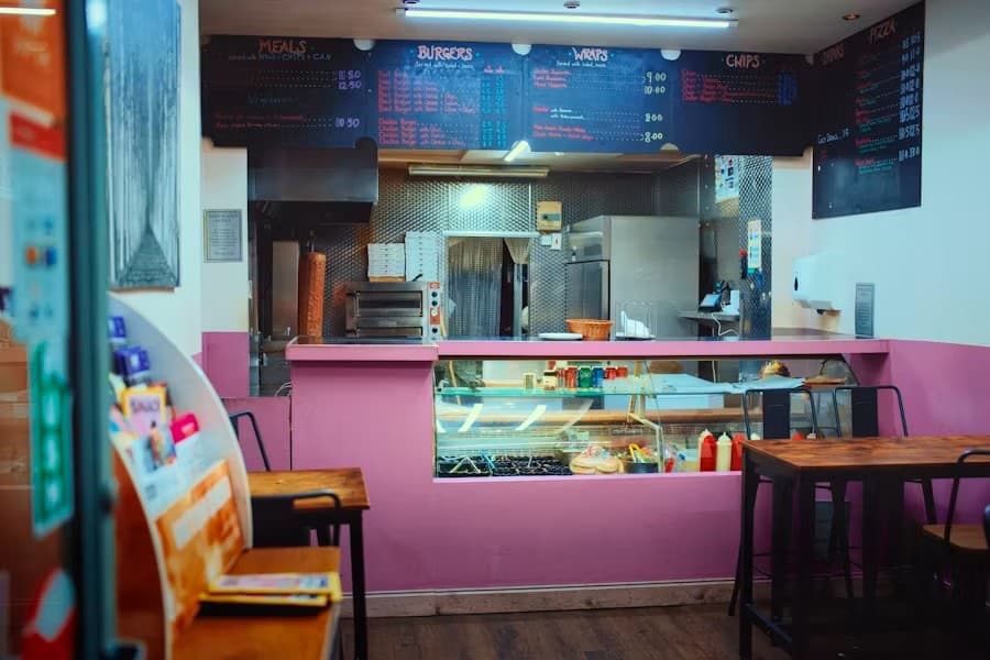 Intérieur d'une boutique kebab : comptoir, broche au fond, menus au tableau, tables vides.
