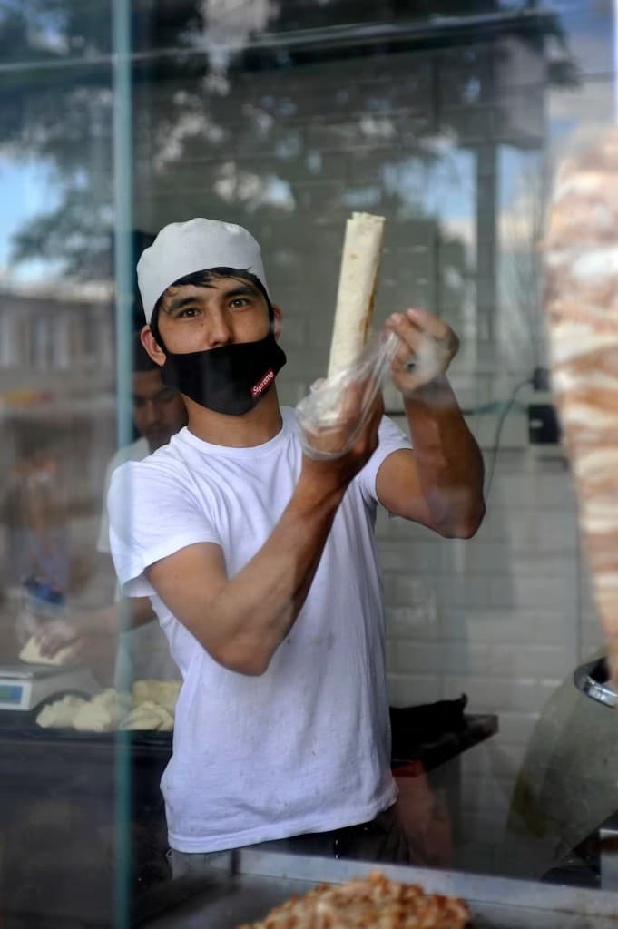 Derrière la vitre, un cuisinier tend un dürüm encore chaud, la broche floue derrière lui.